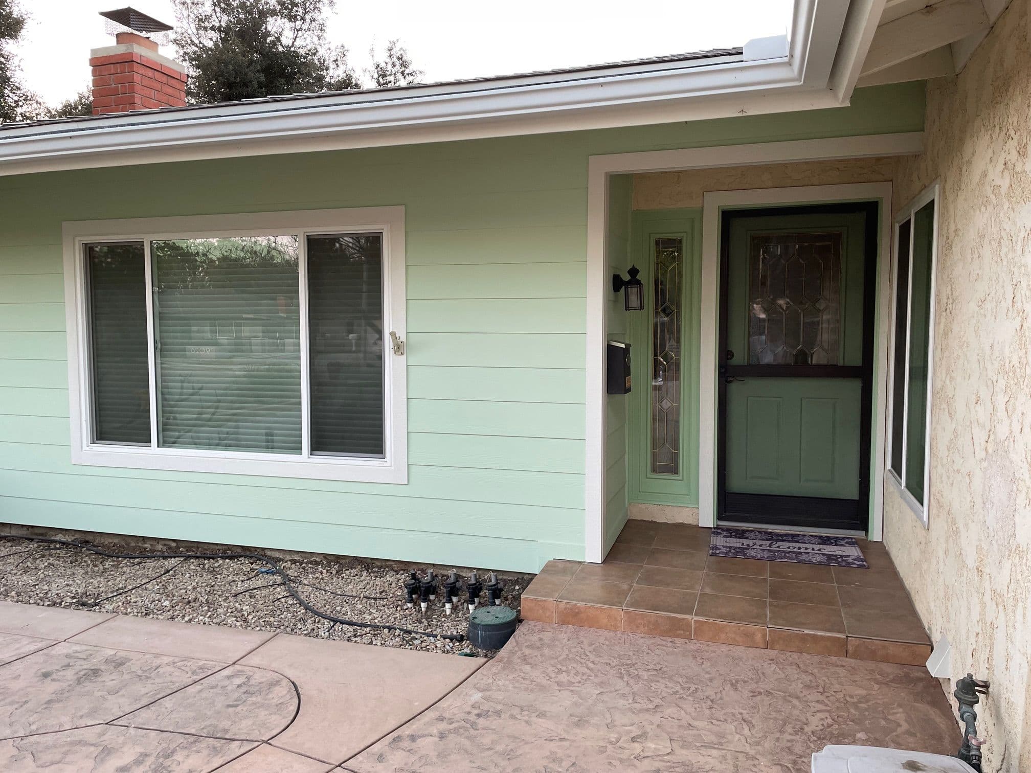 Front entrance of a green house with a porch, large window, and tiled steps.
