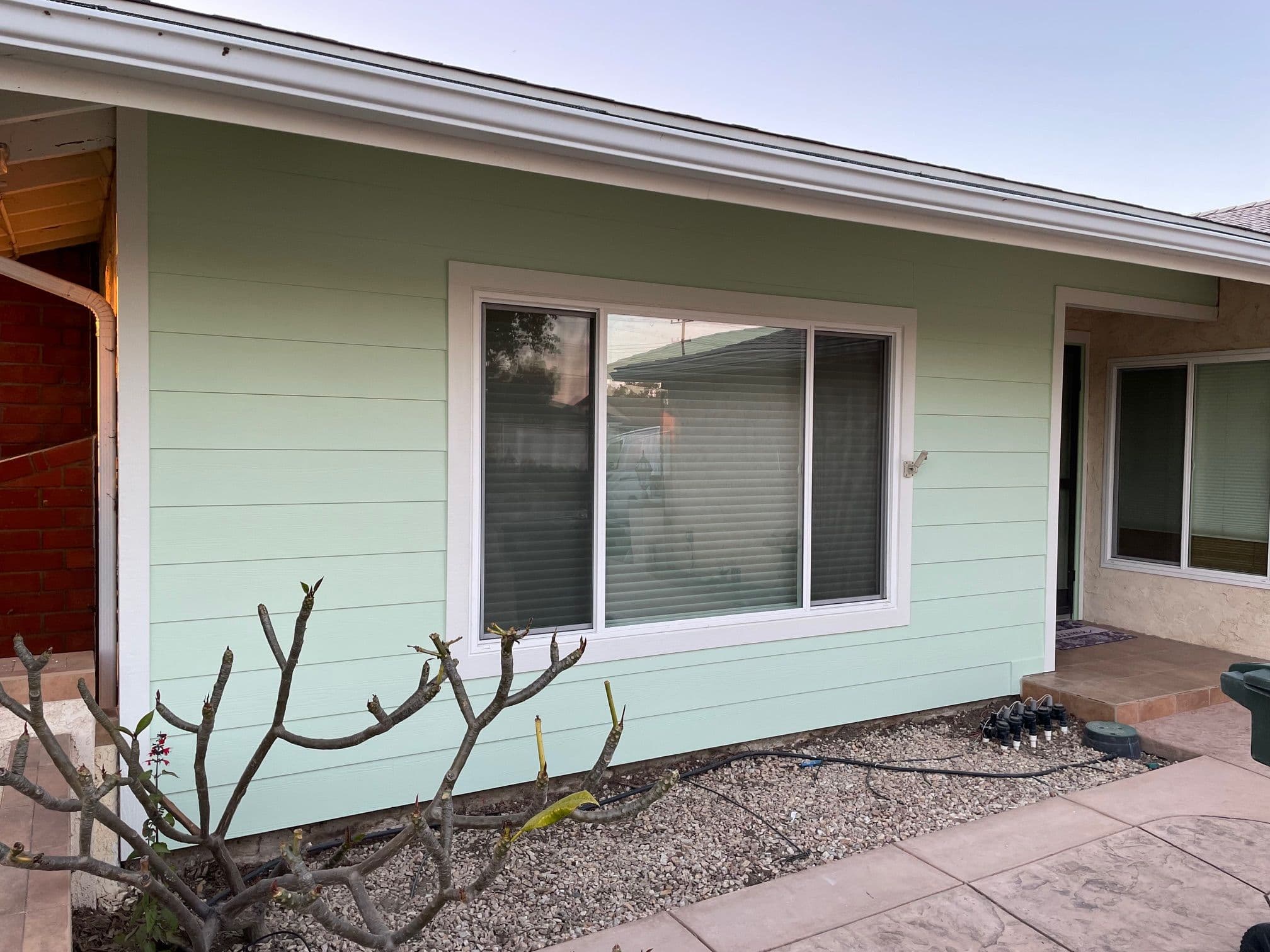Light green house exterior with large window and landscaped yard. Modern architectural design.