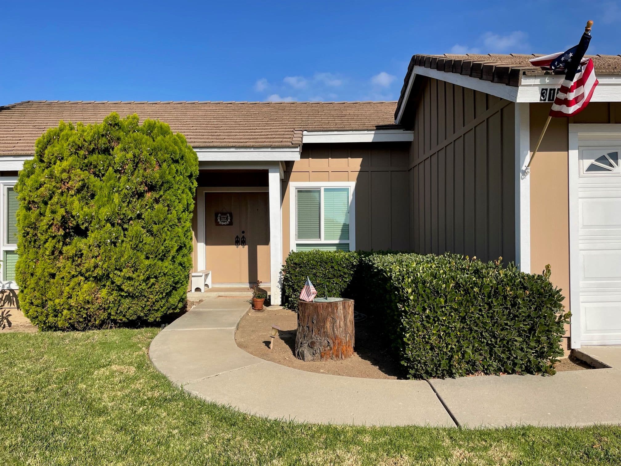 Front view of a suburban home with greenery, a stump, and an American flag on display.